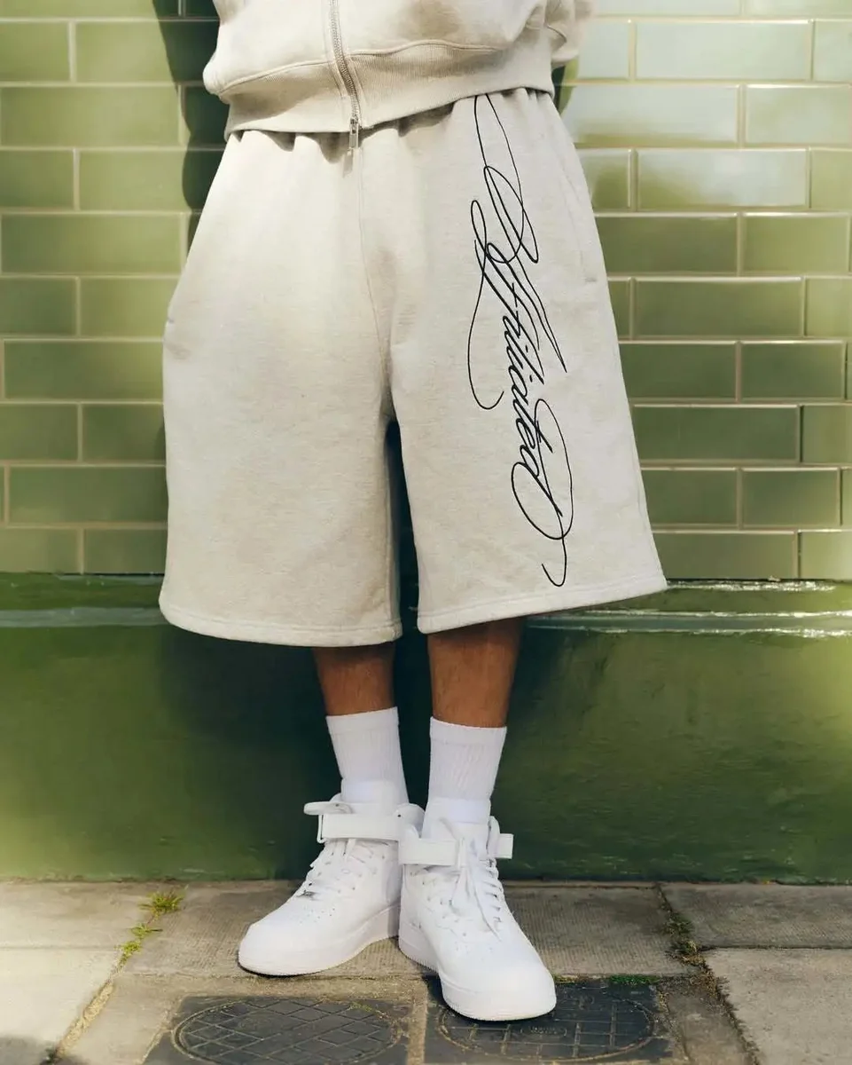 Light-coloured shorts with dark script lettering, shown worn